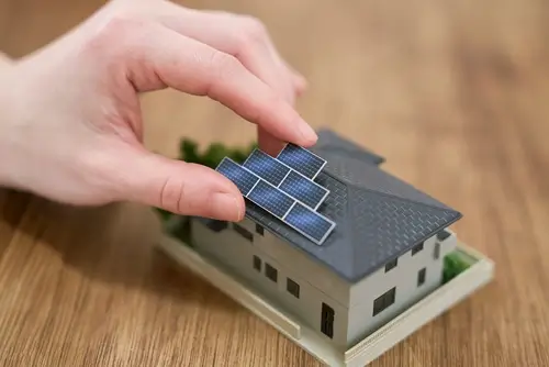 Hand placing miniature solar panels on a model home to represent factors that affect solar costs
